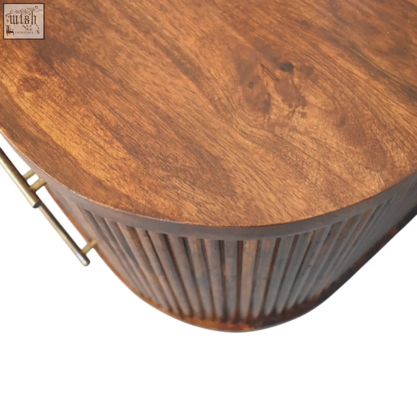 A warm wooden ribbed bedside table with curved top and brass handles on vertical fluted sides