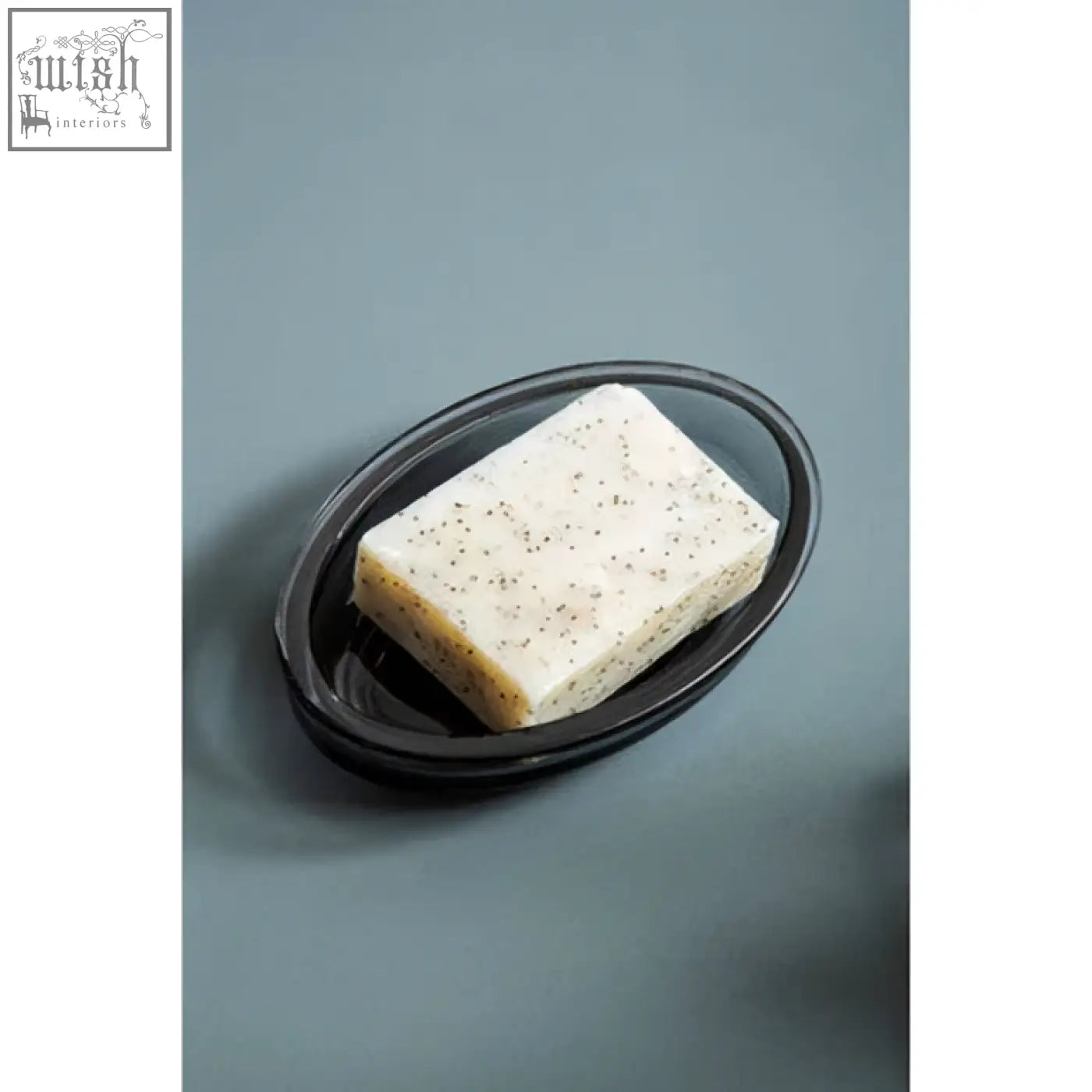 Black oval glass soap dish holding a rectangular off-white speckled soap bar ridley glass soap dish