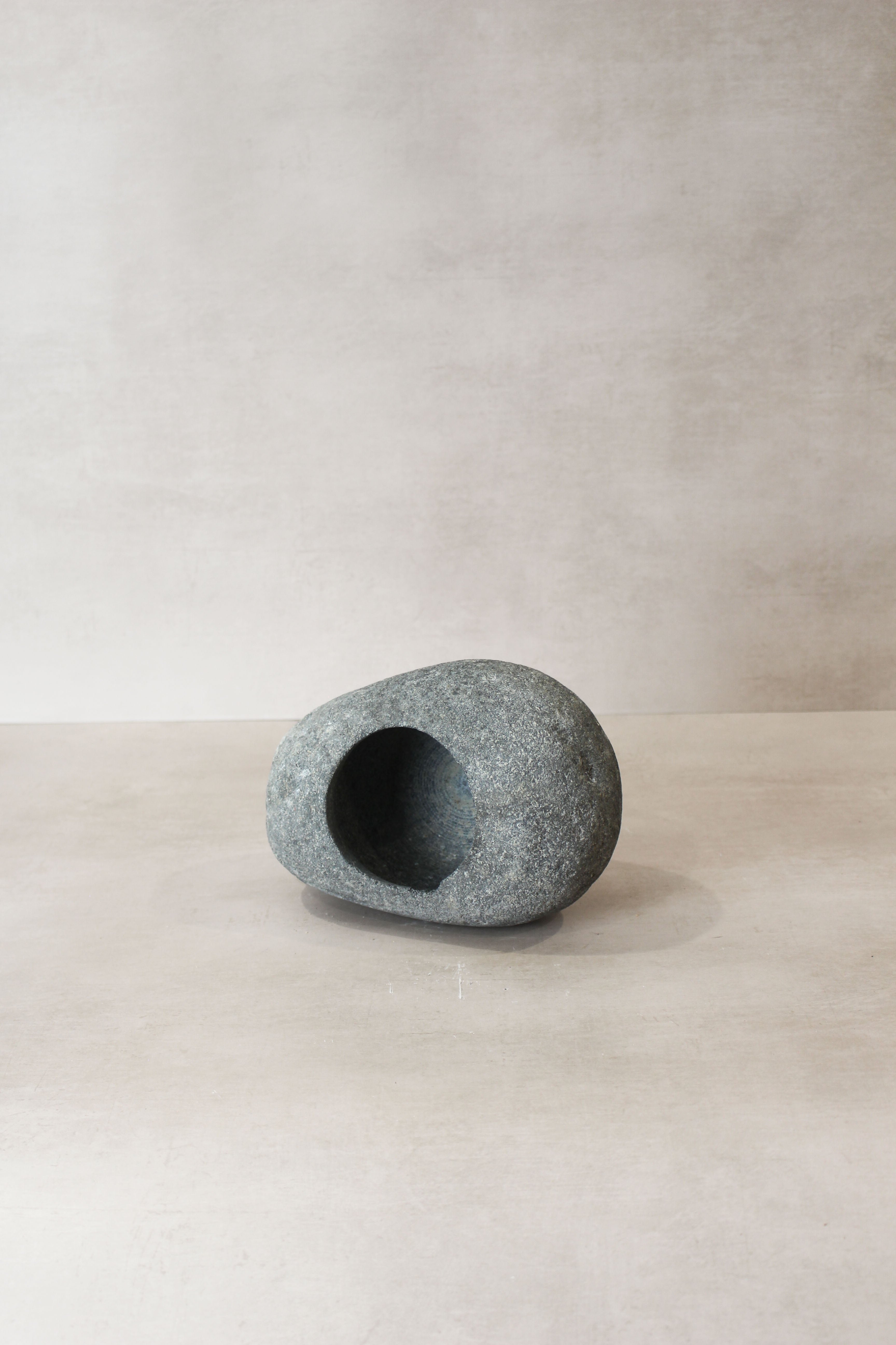 A smooth gray river stone planter pot with a rounded shape and hollowed-out center for plants