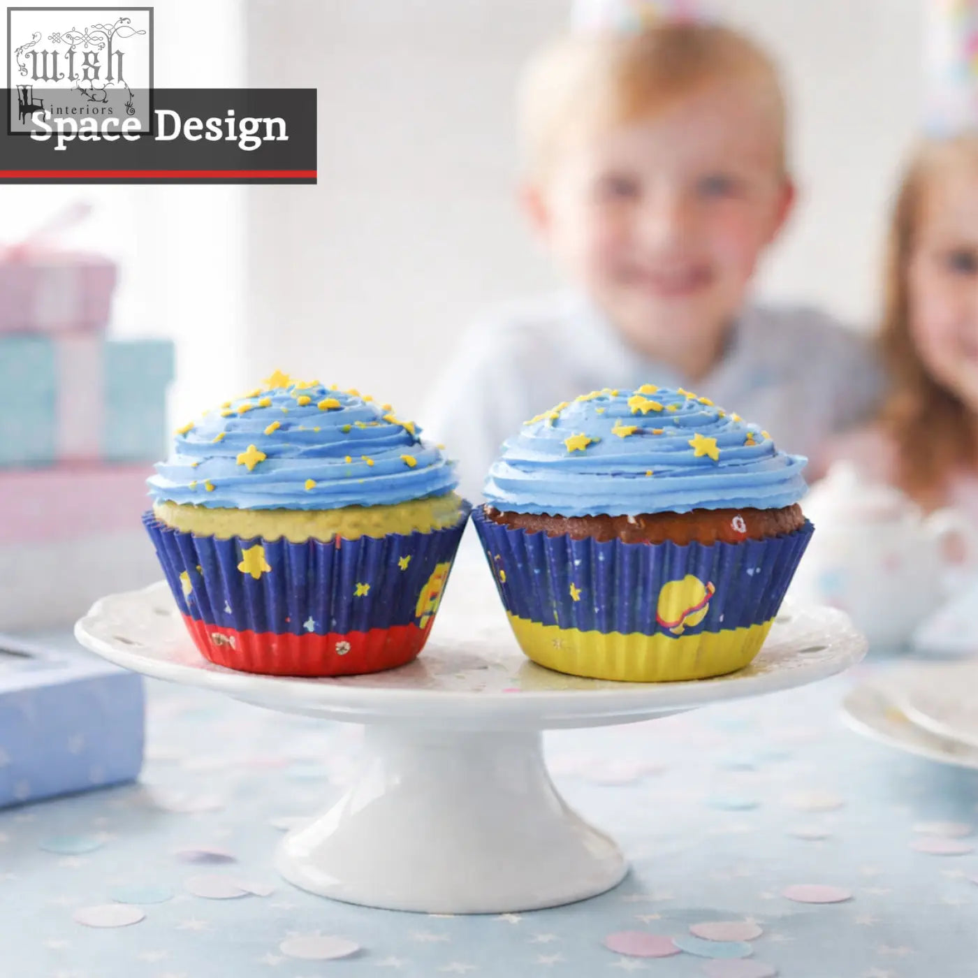 Two cupcakes with blue frosting and yellow star sprinkles in colorful space-themed large cupcake cases