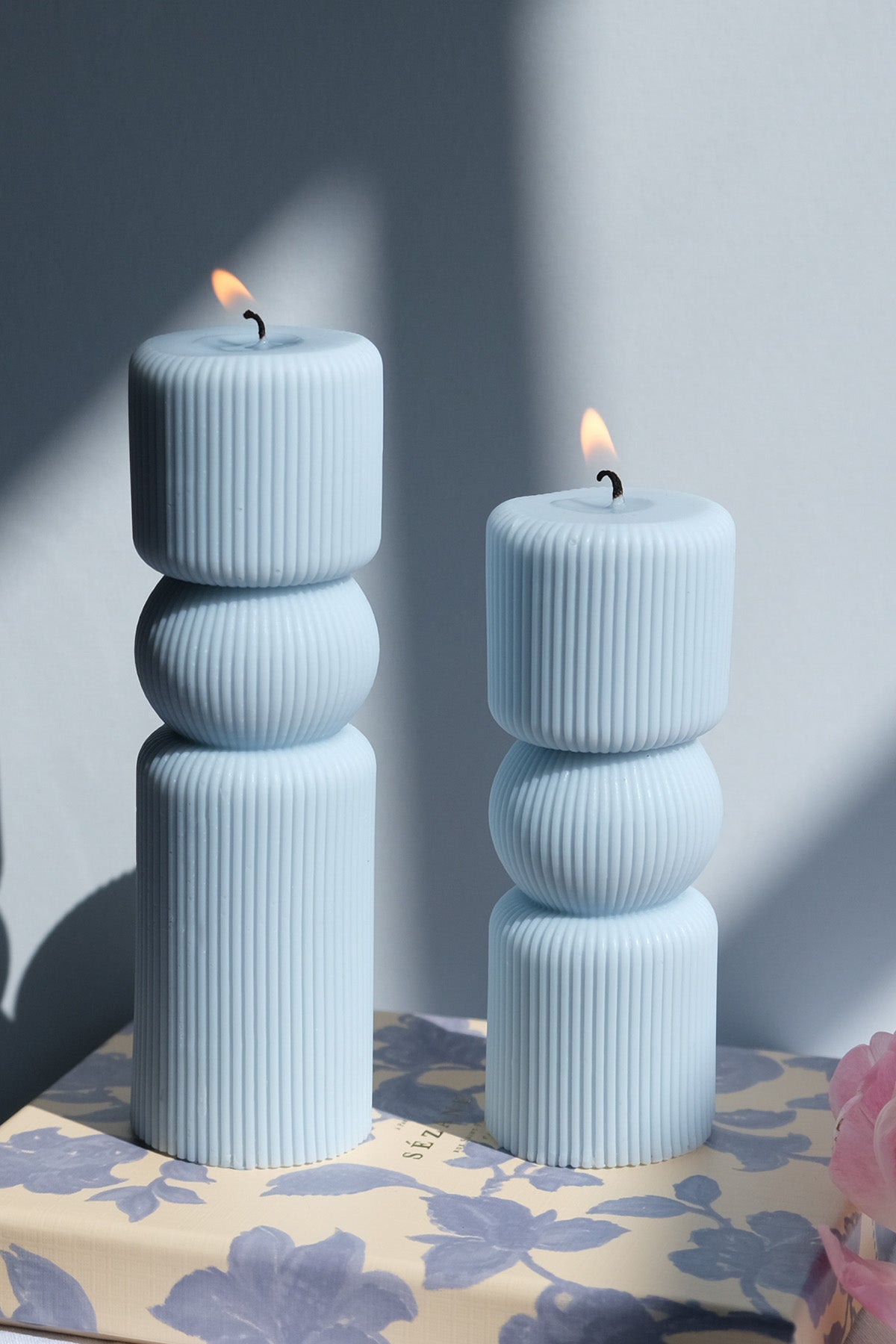 Two light blue roman pillar candles with ribbed texture and lit wicks stacked vertically for elegant decor