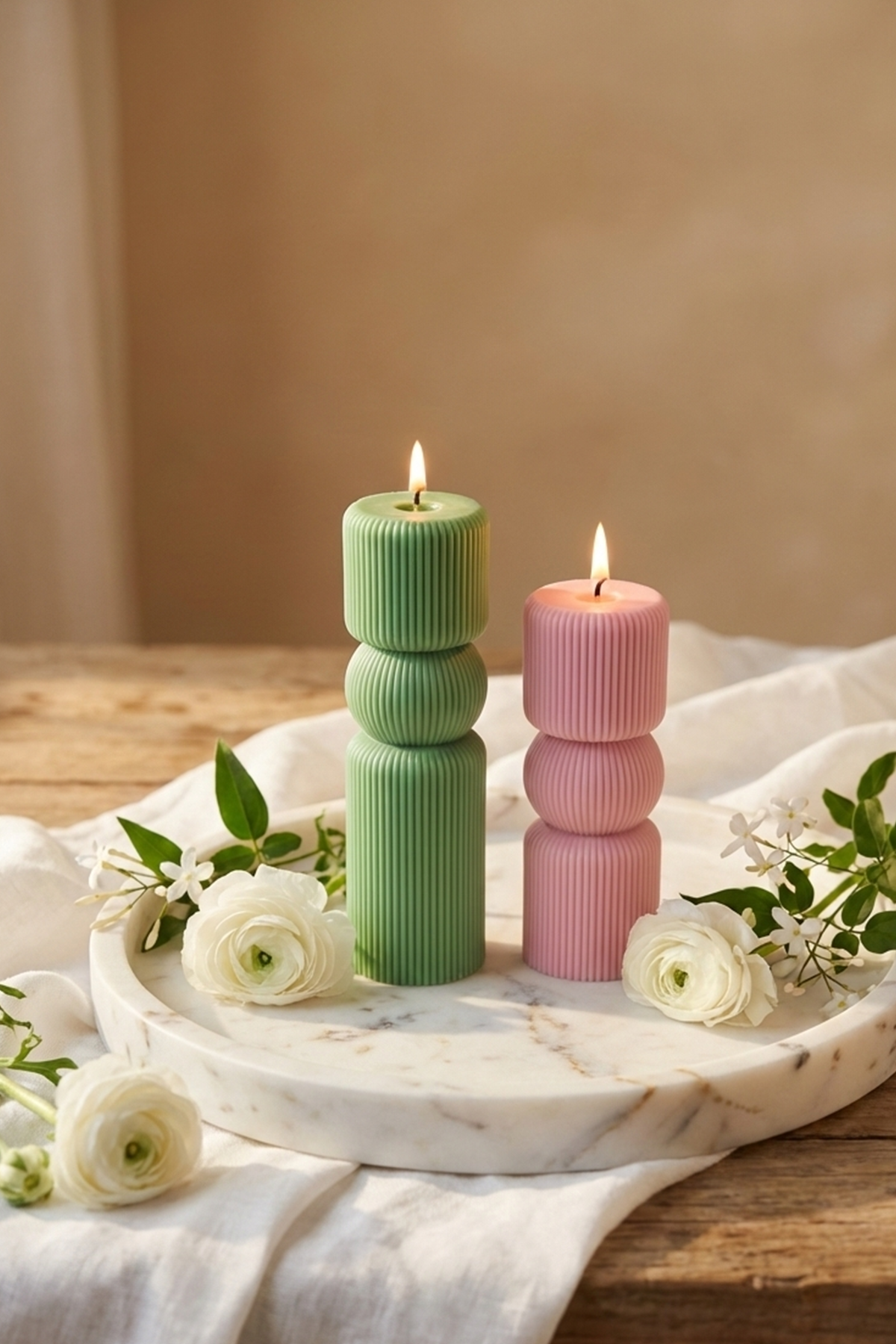 Two lit ribbed roman pillar candles in soft green and blush pink on a marble tray for cozy decor