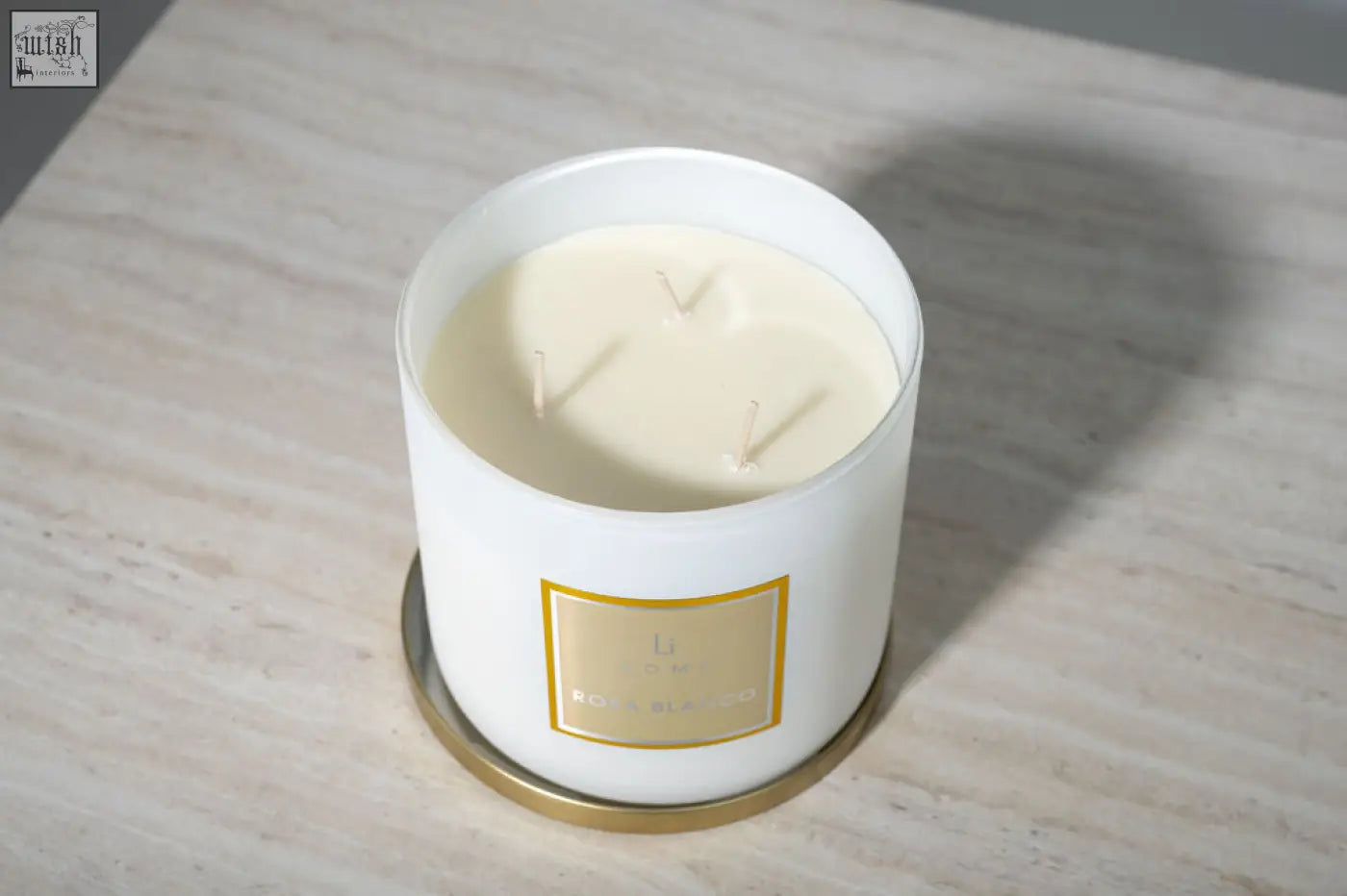 White cylindrical large candle in glass jar with gold foil label and three wicks from l’occitane candle collection