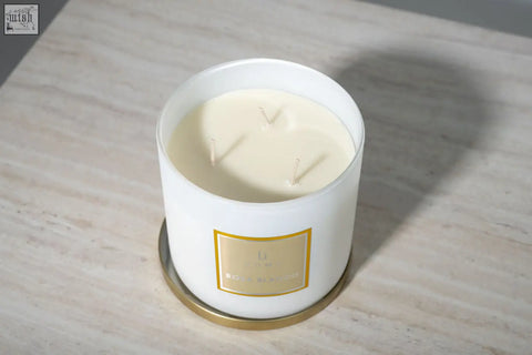 White cylindrical large candle in glass jar with gold foil label and three wicks from l’occitane candle collection