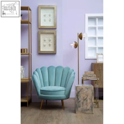 A teal velvet shell-shaped armchair with gold-tone legs paired with a rosado marble effect side table and stool