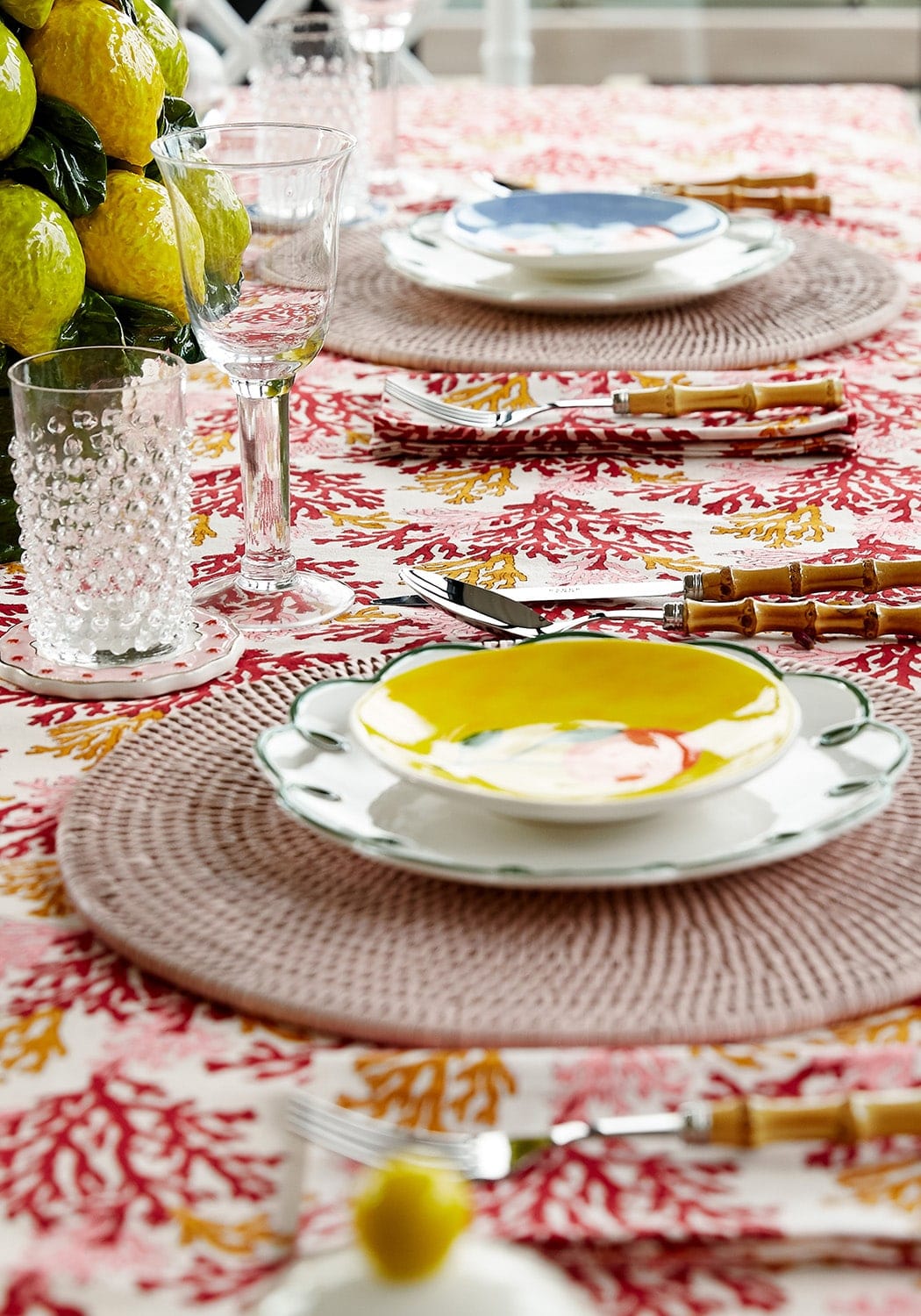 Yellow ceramic bowl with white interior and green rim on matching plate paired with rose coral table napkin set of 4