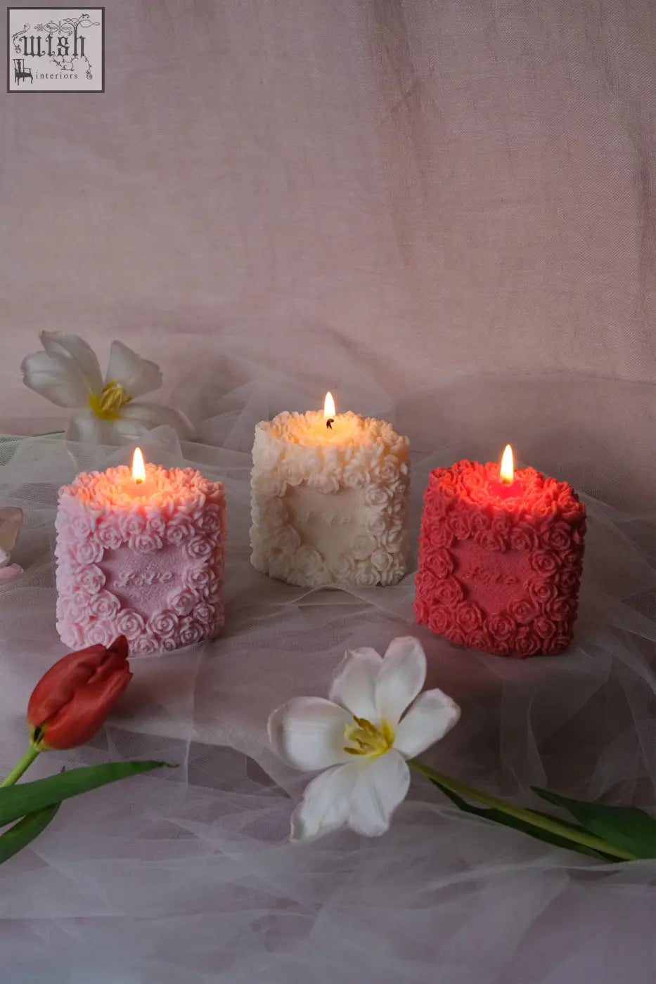 Three lit square-shaped rose pillar candles with love embossed and detailed rose designs on the front