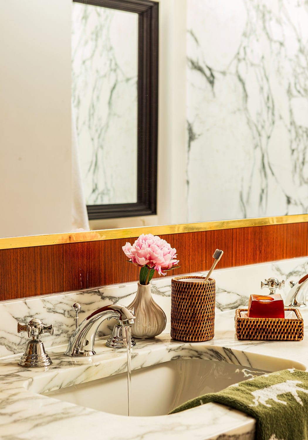 A pink peony flower in a matte ceramic vase next to rosies suds and style rattan soap dish for stylish storage