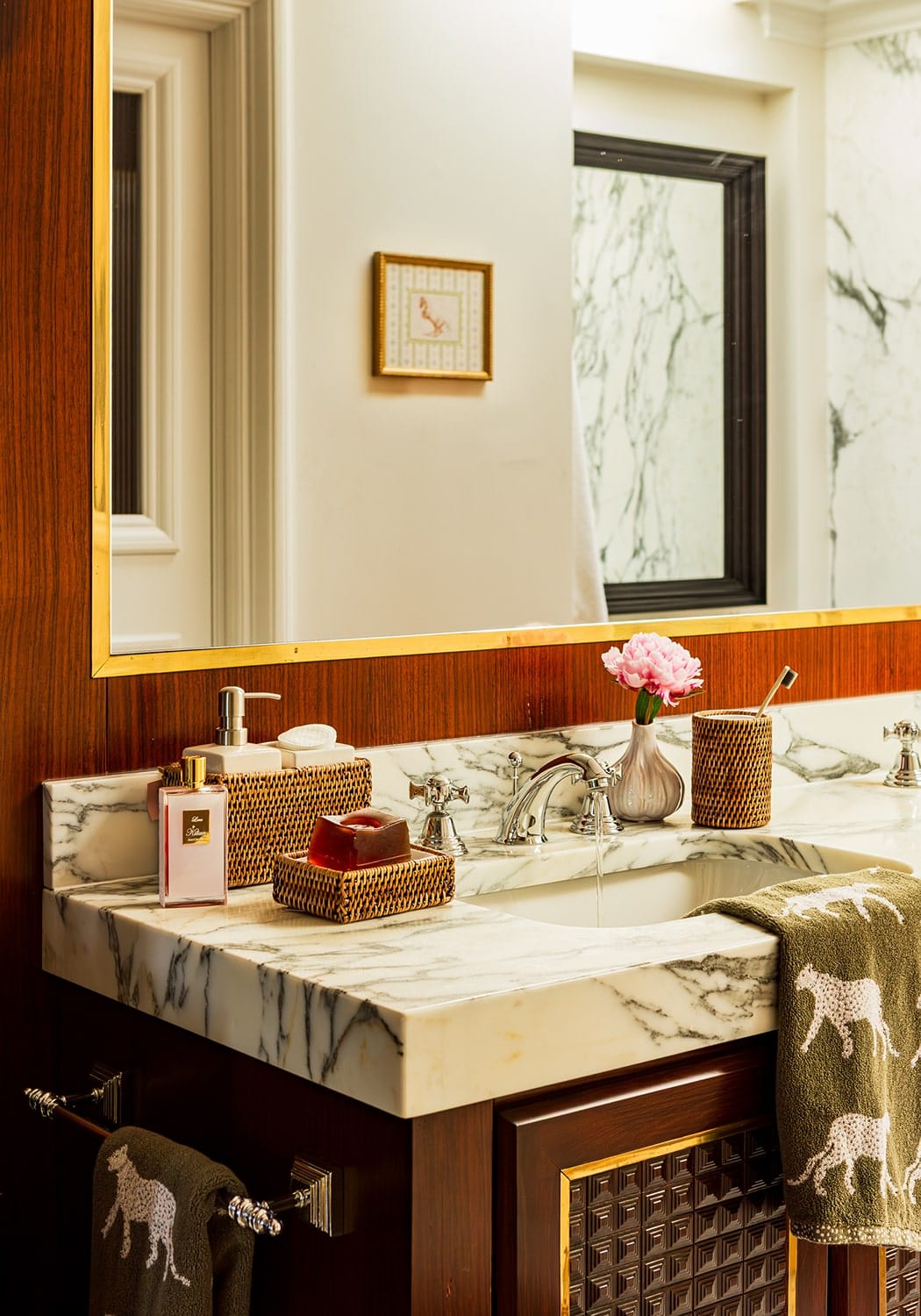 A sleek white marble sink with dark veining on a wood vanity paired with rosies suds and style rattan soap dish