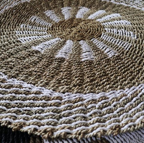 A hand-crocheted round seagrass mat in white and tan with a sunburst pattern measuring 1 meter across