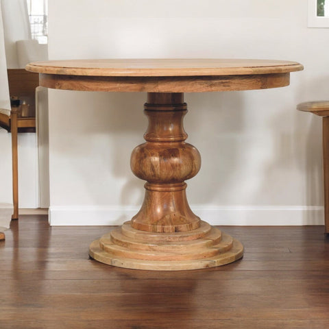 Rustic round turned dining table with thick natural wood finish and ornate stacked circular pedestal base