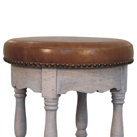 Rustic charm stool with brown leather top, distressed gray wooden legs, and brass nailhead trim