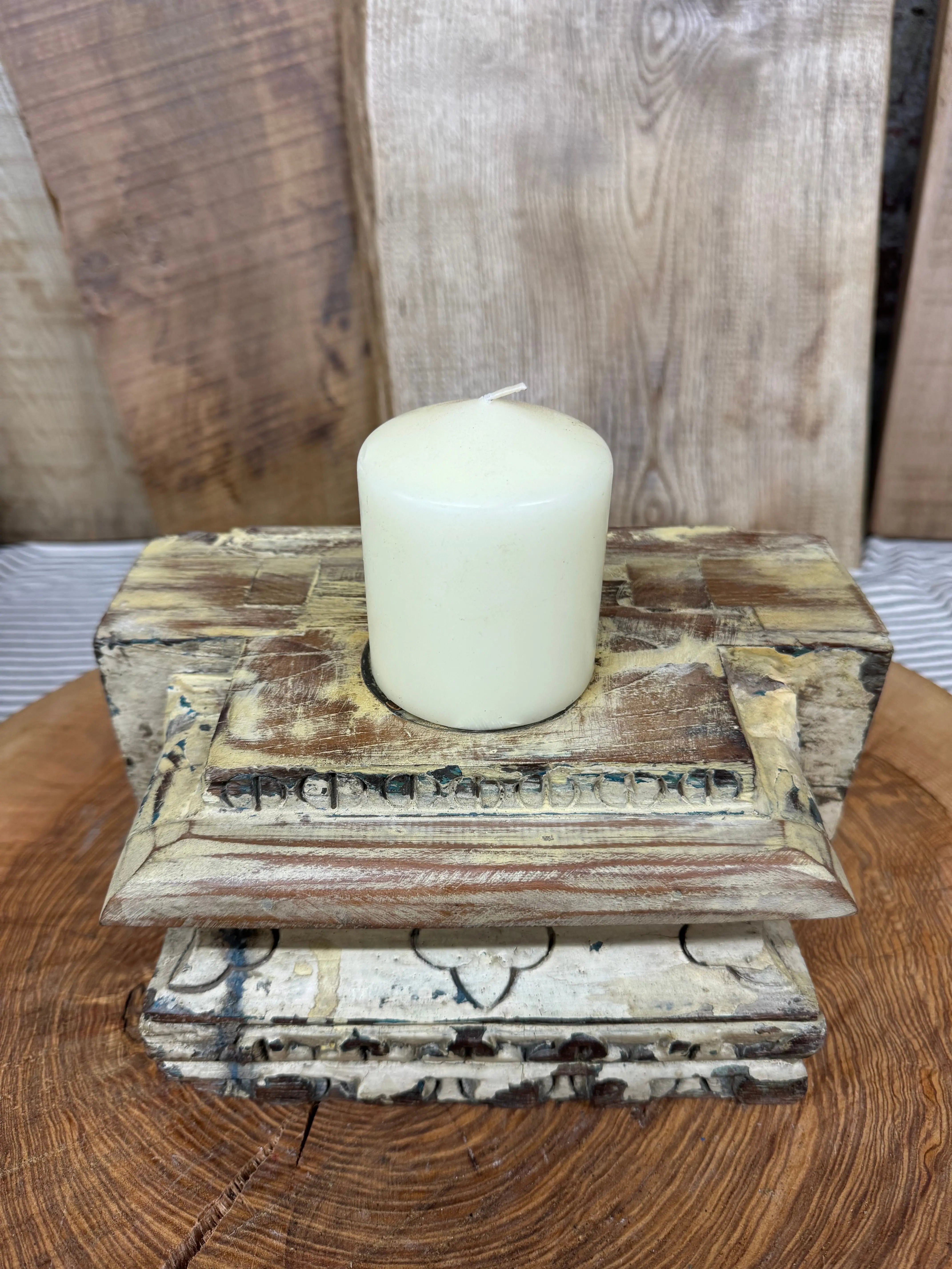 Cream candle resting in rustic church candle holder indian pillar base with distressed wood and carved details