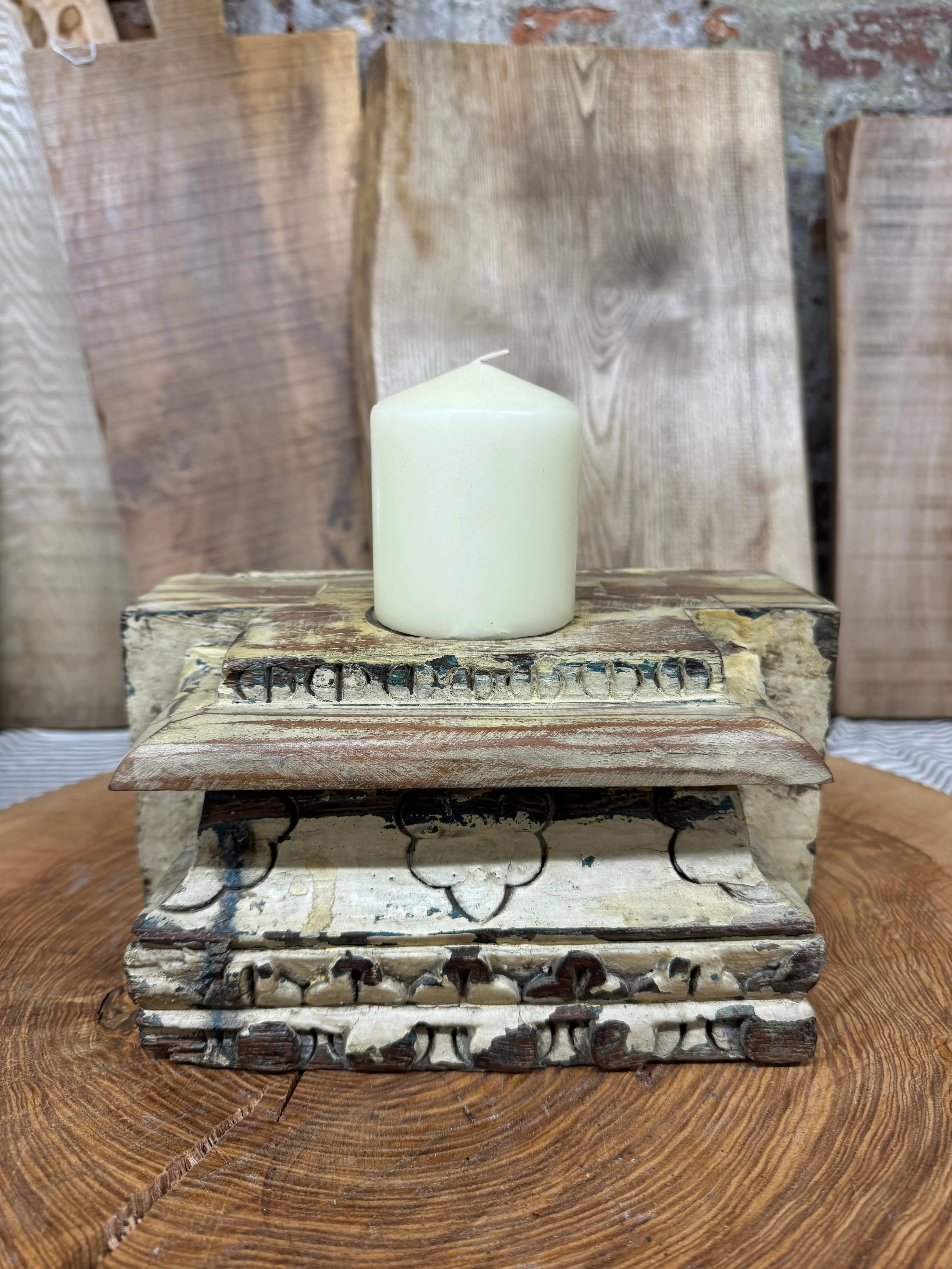 A cream candle sits on a weathered wooden indian pillar base candle holder with peeling paint for farmhouse decor