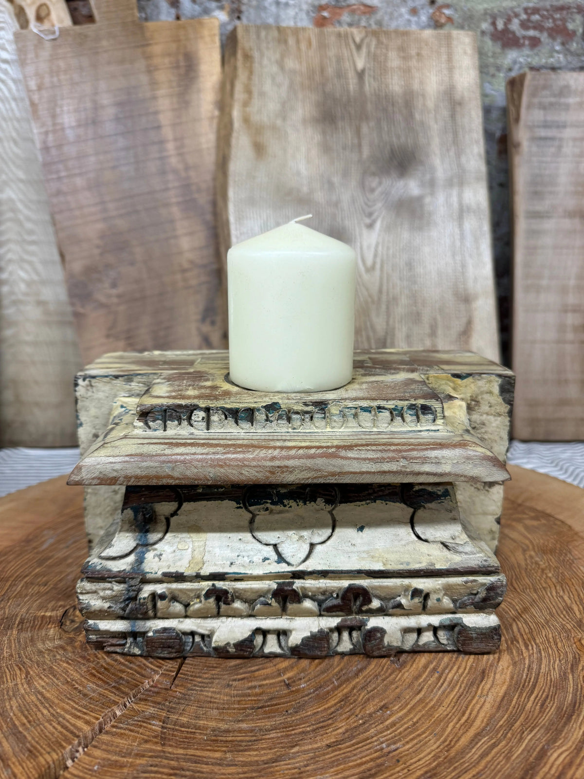A cream candle sits on a weathered wooden indian pillar base candle holder with peeling paint for farmhouse decor