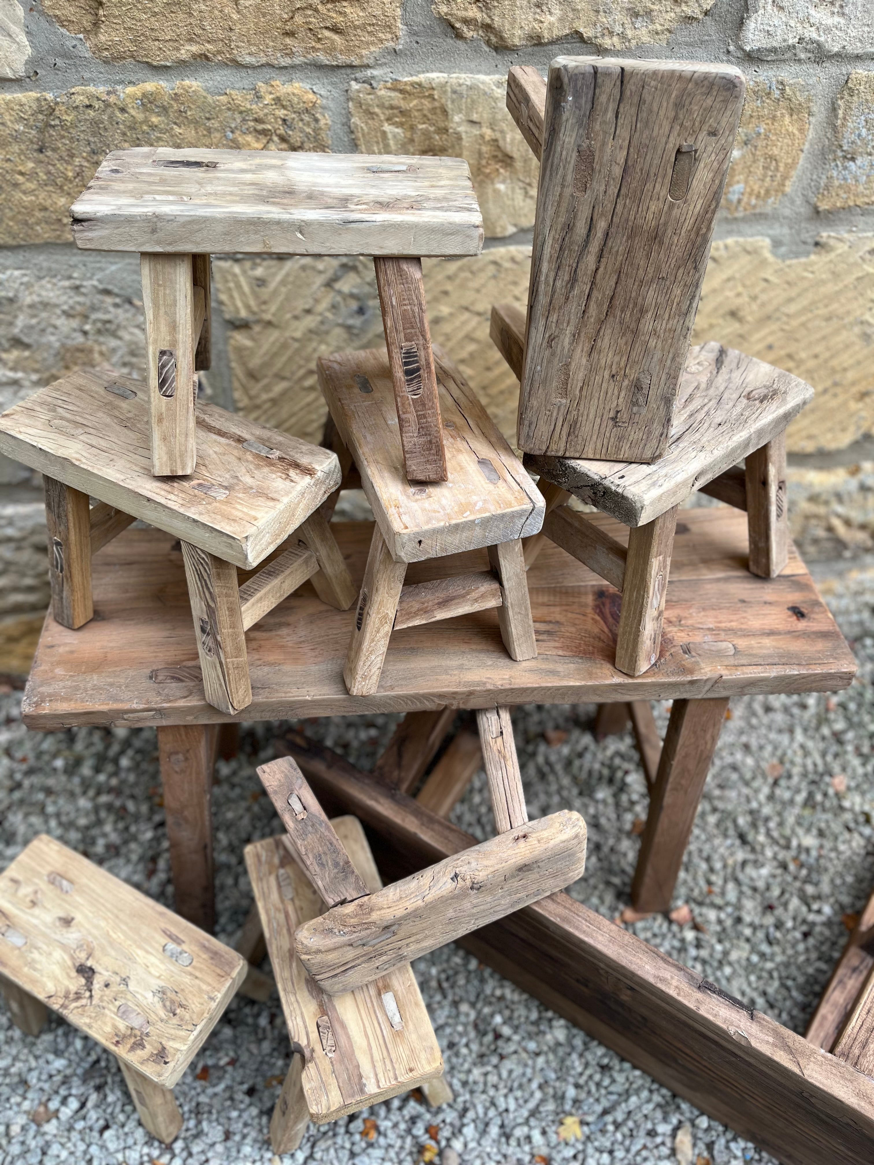 Rustic elm bench with weathered natural wood grain and varied light to medium brown tones on wooden stools