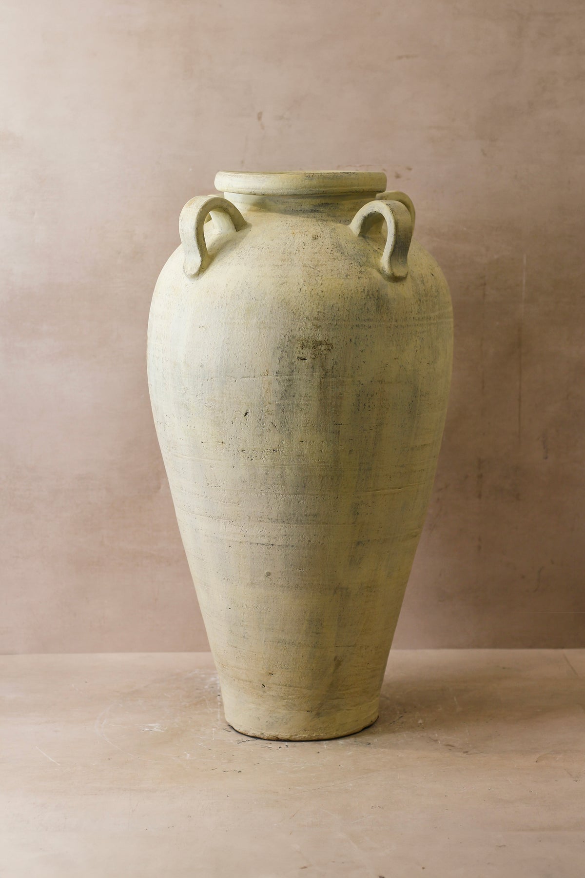 A tall off-white rustic indonesian pot made of ceramic with two looped handles perfect for decor or kitchen use