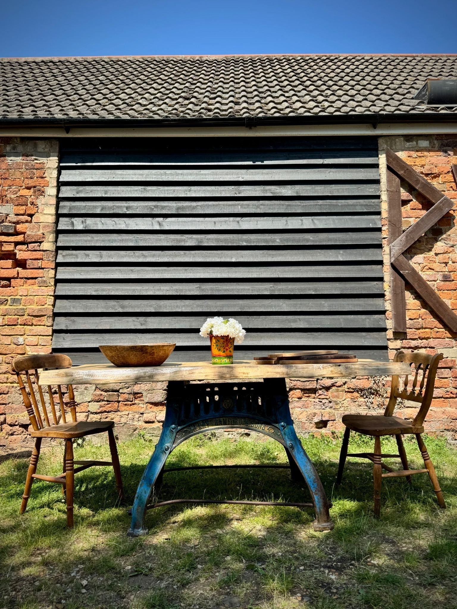 Rustic industrial table with solid ash top and blue cast iron base flanked by two wooden chairs for kitchen use