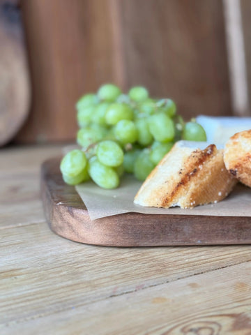 A rustic wooden chopping board with fresh green grapes and toasted bread slices for antipasti and charcuterie