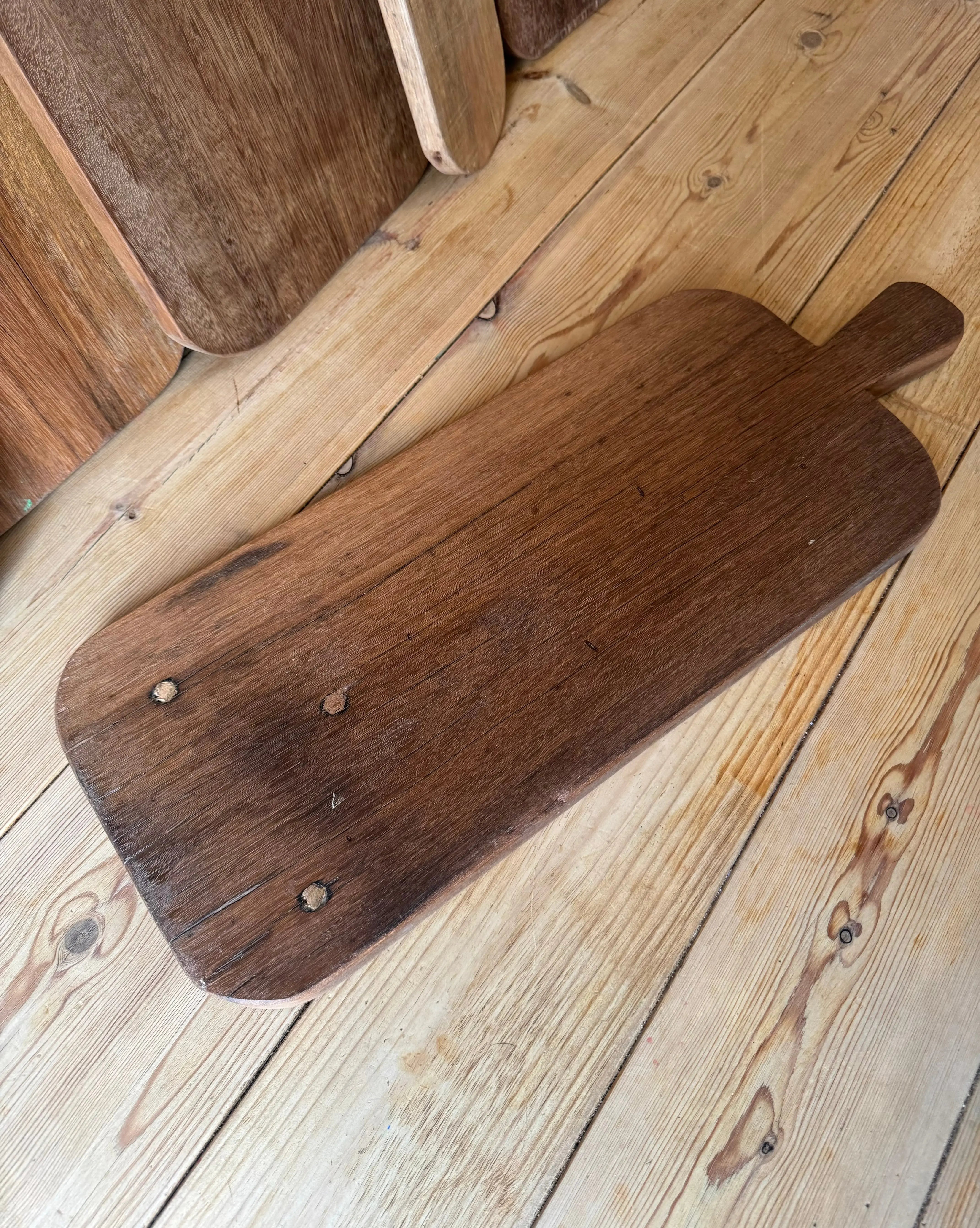 Dark brown wooden chopping board with handle and metal fasteners perfect for rustic cheese or charcuterie serving
