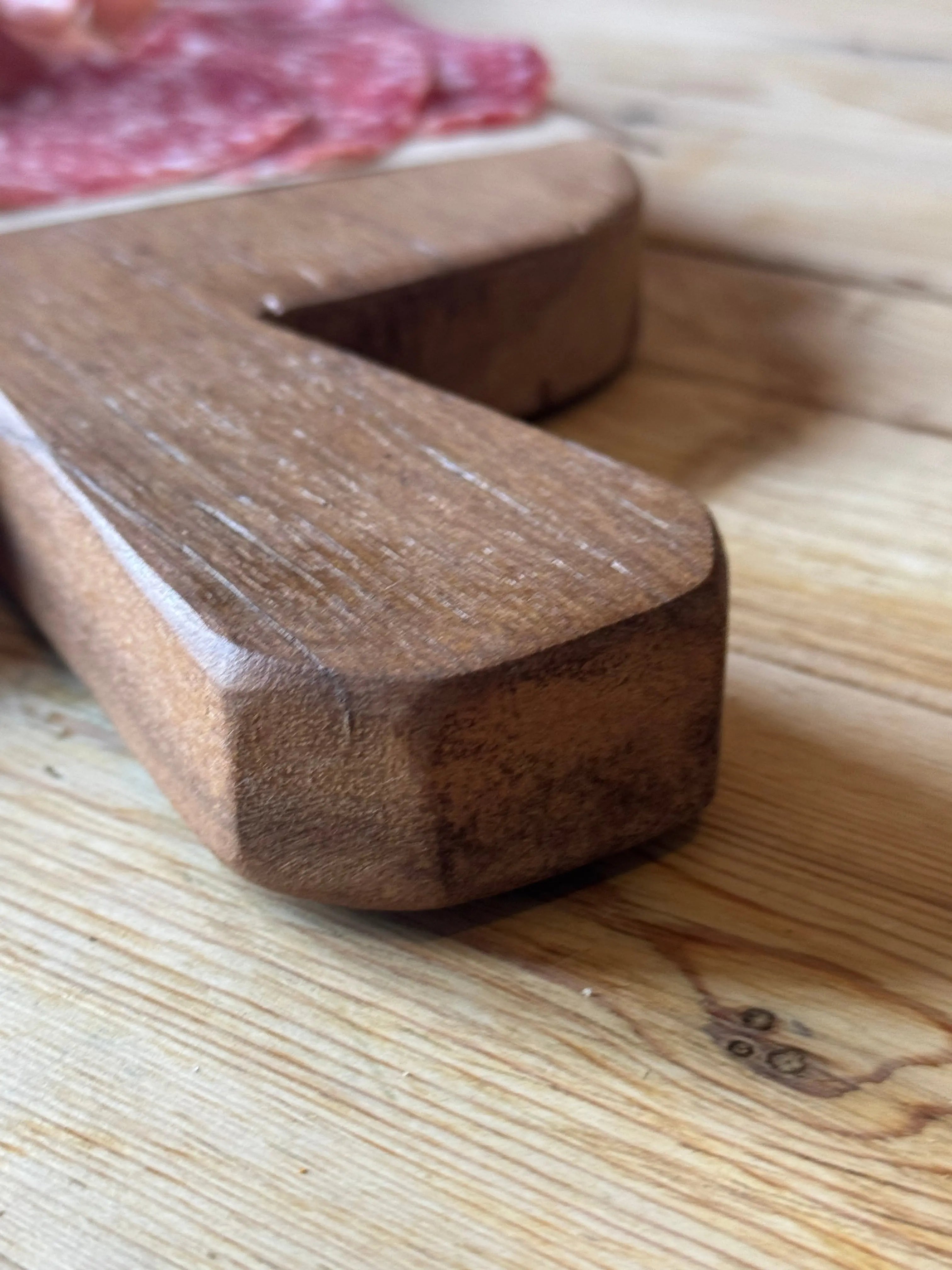 Rustic dark brown wooden chopping board shaped like letter z with smooth slightly worn finish for cheese and charcuterie