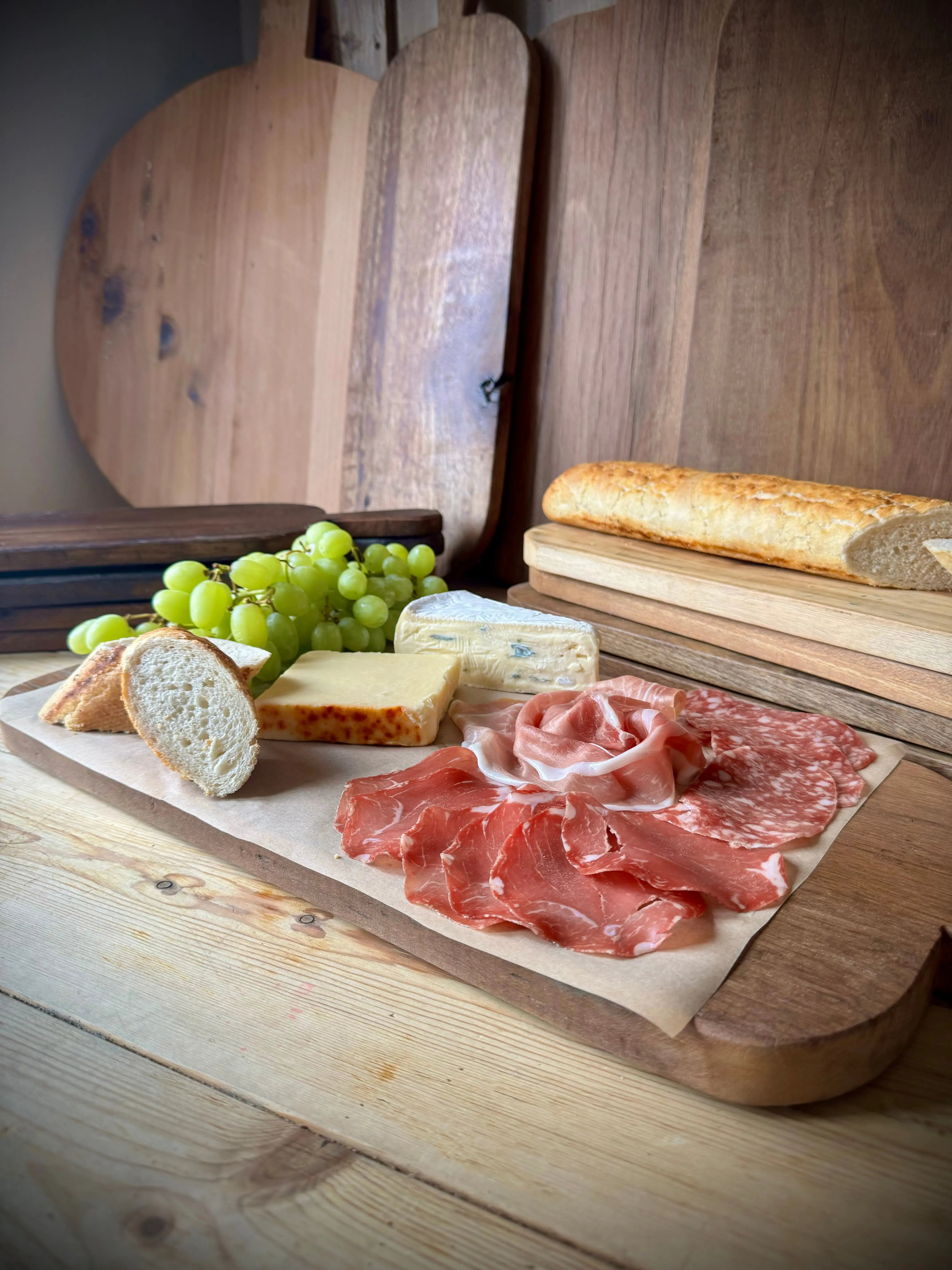Rustic wooden chopping board with a natural finish holding cheeses cured meats and fresh grapes for antipasti