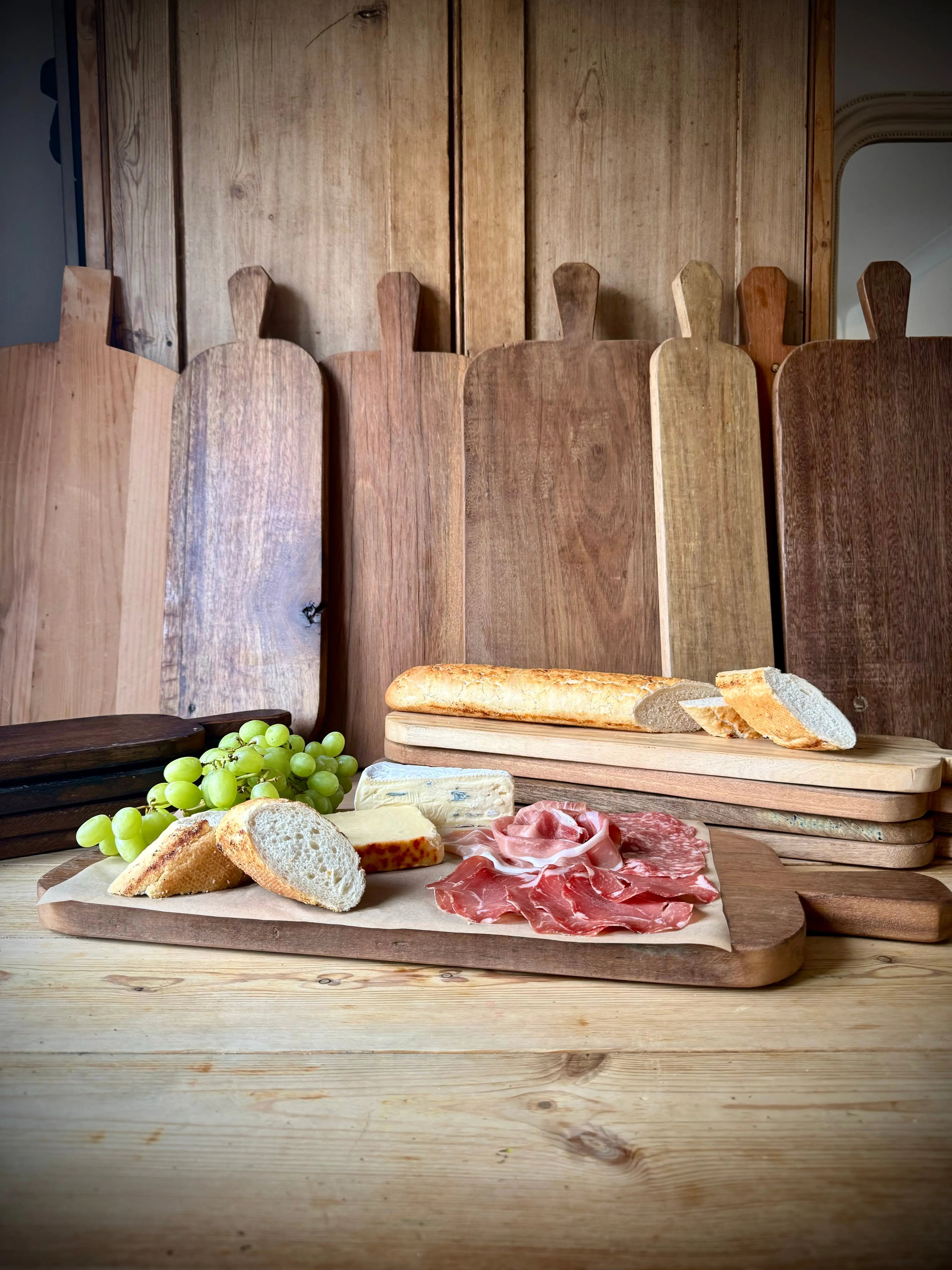 Rustic wooden chopping board with natural wood grain and handle displaying cheeses cured meats bread and grapes