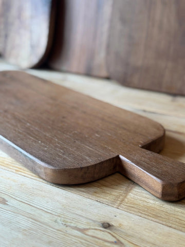 Rustic dark brown wooden chopping board with smooth rounded handle and natural wood grain for cheese and charcuterie
