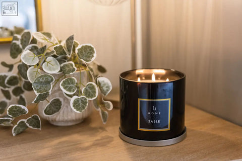 Black cylindrical sable 3 wick luxury candle with gold rim and label lit in a large candle collection