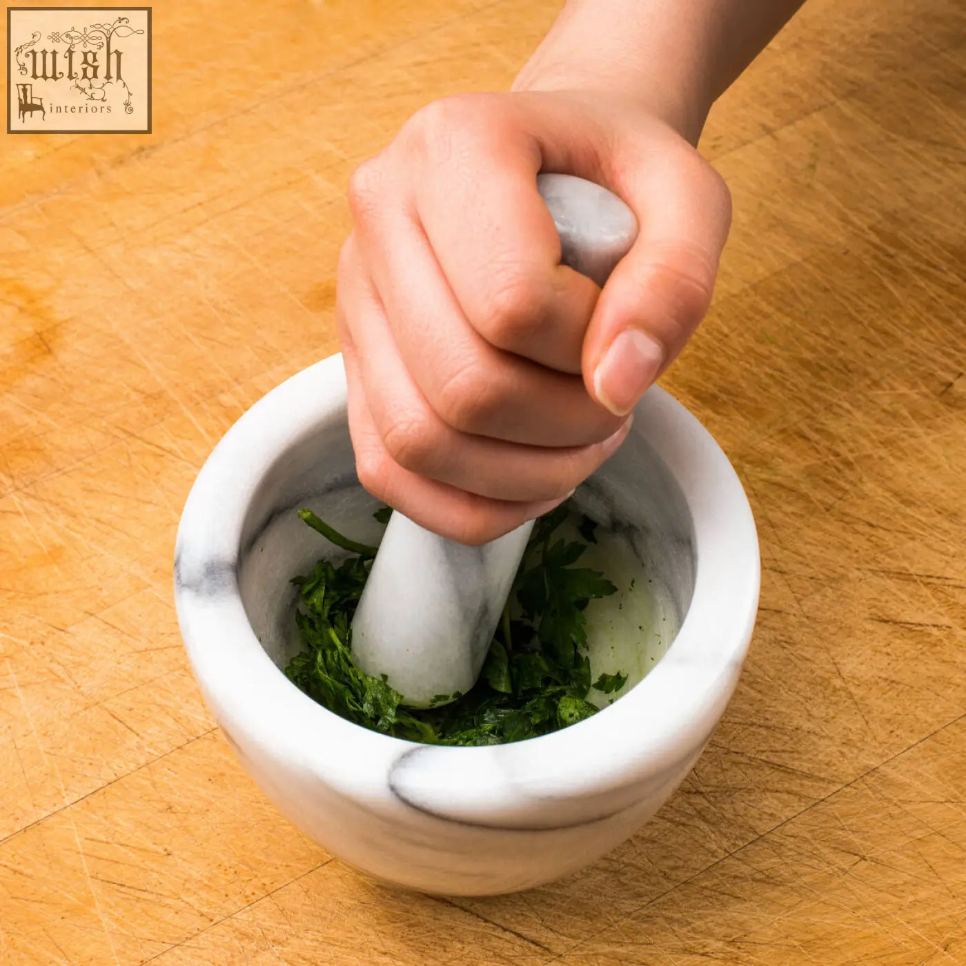 Salerno white marble mortar and pestle set with green herbs inside showing a white marble mortar in use