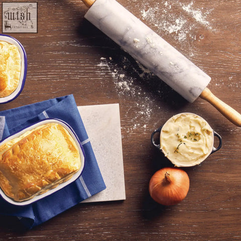 Golden brown pie in a white enamel dish on navy cloth with salerno white marble rolling pin with wooden handles nearby