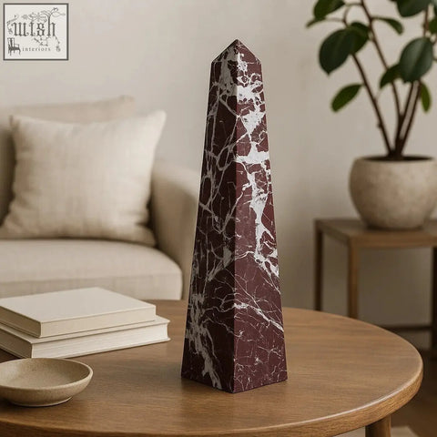 A sleek salmo large red marble obelisk with intricate white veining stands on a wooden table