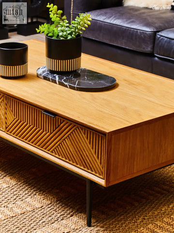 Light wood coffee table with geometric front panel and black metal legs next to salmo oval black marble chopping board