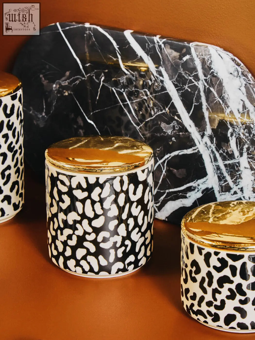 Black and white leopard print ceramic canisters with gold lids beside a salmo oval black marble chopping board