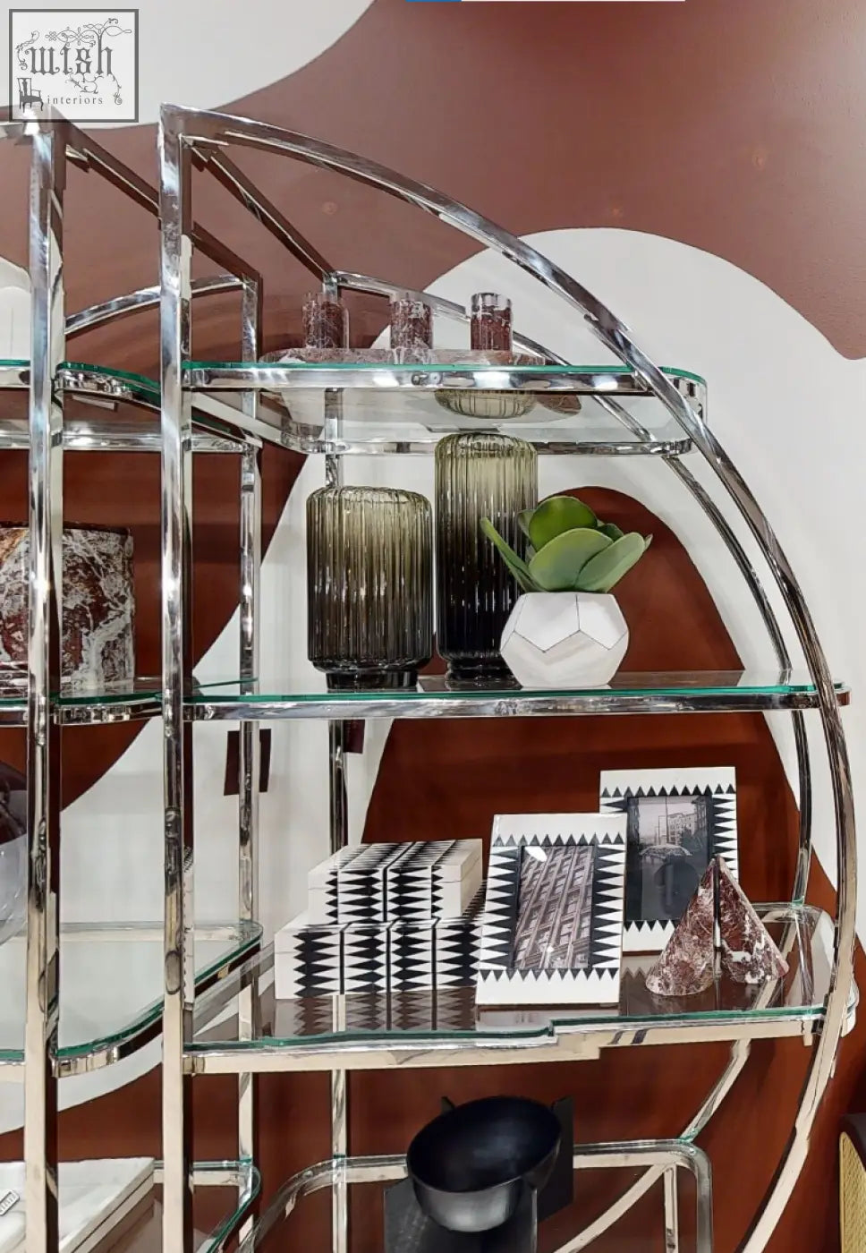 A sleek chrome shelving unit with glass shelves displays three red marble tealight holders and decorative vases