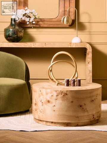 A round burl wood coffee table with natural grain and two gold rings next to three red marble tealight holders