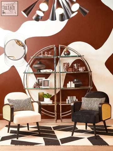 A modern circular glass shelving unit with a metallic frame showcasing three red marble tealight holders and books