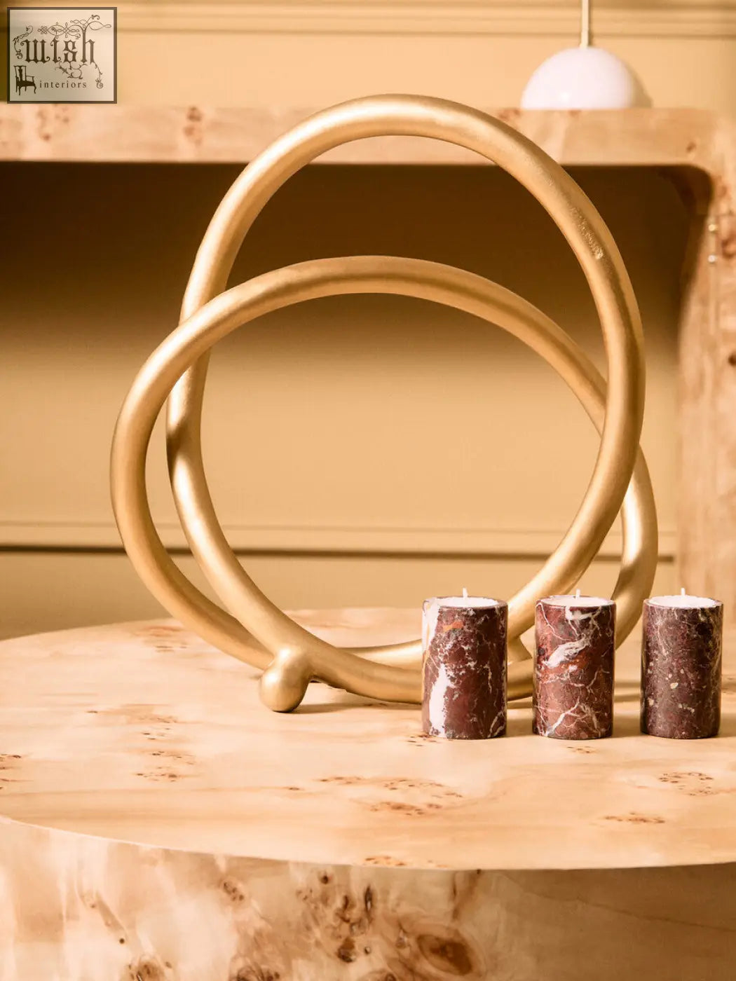 Golden metallic sculpture with interlocking rings on a spherical base shown with three red marble tealight holders
