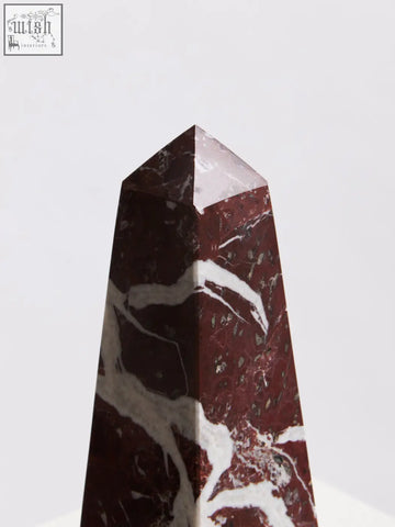 A polished salmo small red marble obelisk with white accents and a pointed top perfect for decor displays