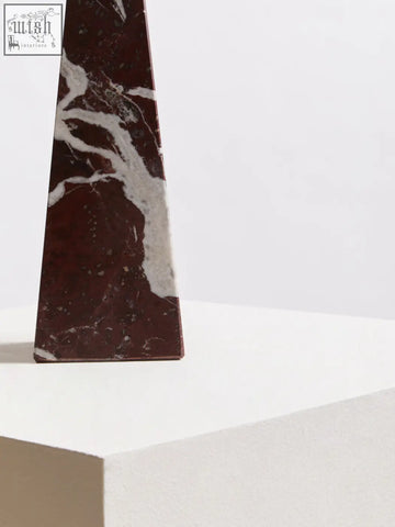 A sleek salmo small red marble obelisk with swirling white veining on a minimalist pedestal