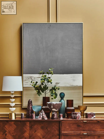 A sleek modern table lamp with a white conical shade and gold-toned bases next to a salmo small red marble obelisk