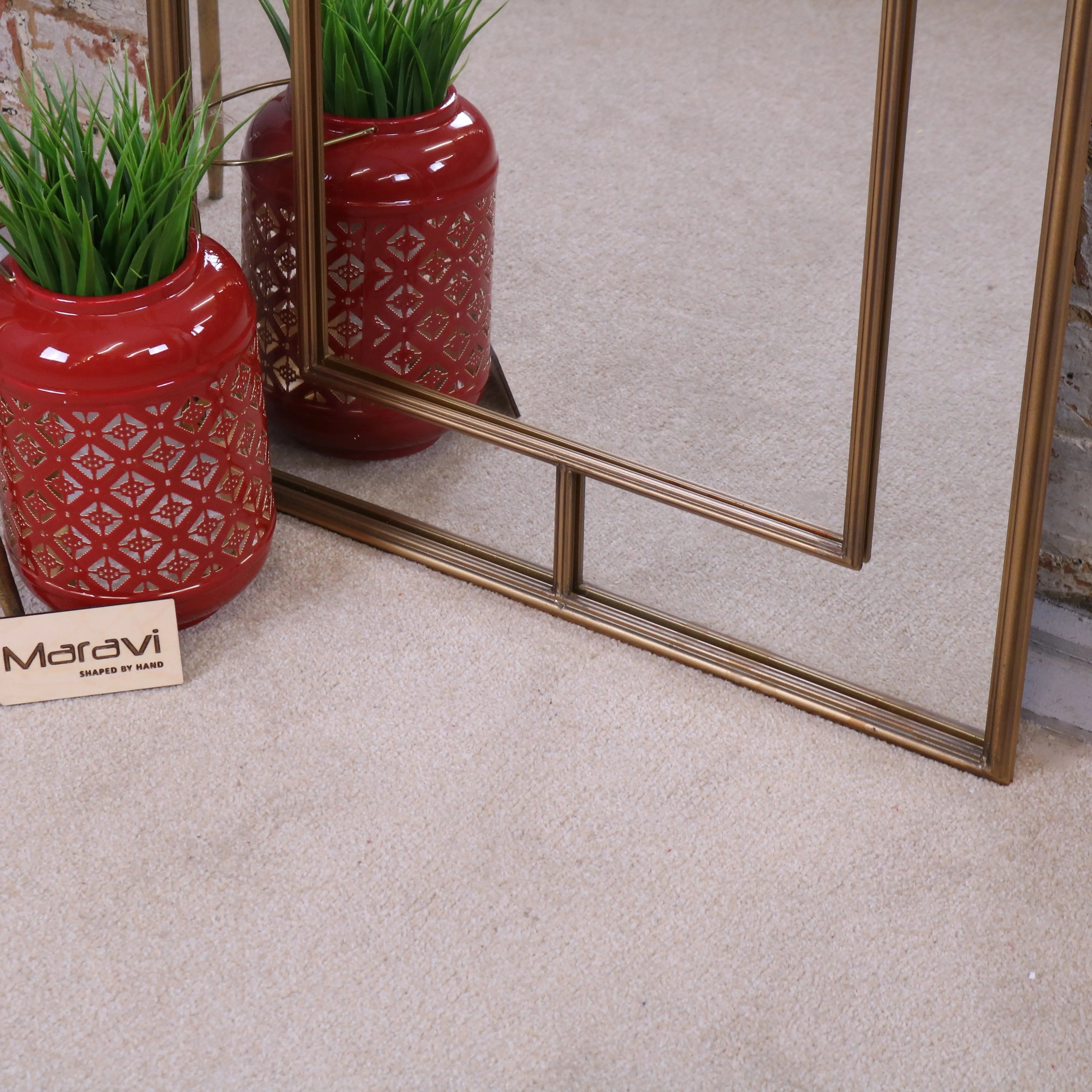 A glossy red ceramic vase with geometric pattern holding green artificial grass next to samela full length arch mirror