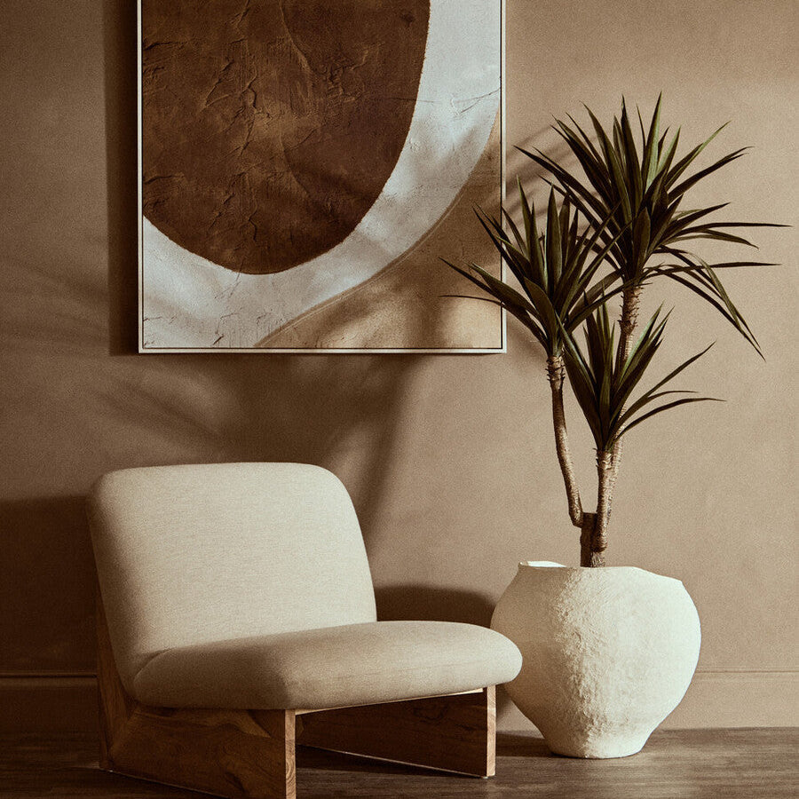 Beige upholstered lounge chair with wooden frame next to large beige planter sanai cotton mache style