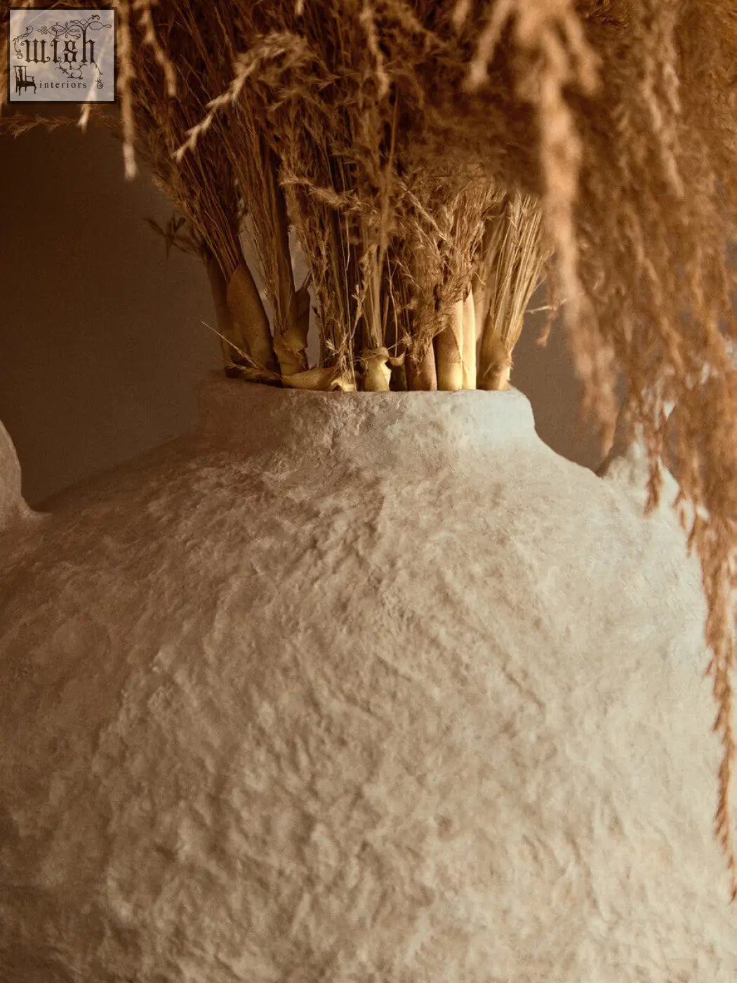 A large sanai cotton mache vase with decorative handles in off-white textured ceramic holding dried grasses