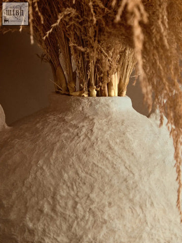 A large sanai cotton mache vase with decorative handles in off-white textured ceramic holding dried grasses