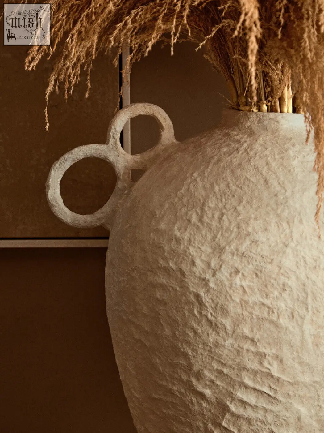 Off-white sanai cotton mache large vase with decorative interlocking ring handles holding dried pampas grass