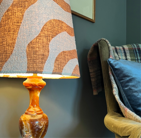 A warm amber glass lamp with a swirling base and an extra tall sandstone wiggle cone lampshade with abstract pattern