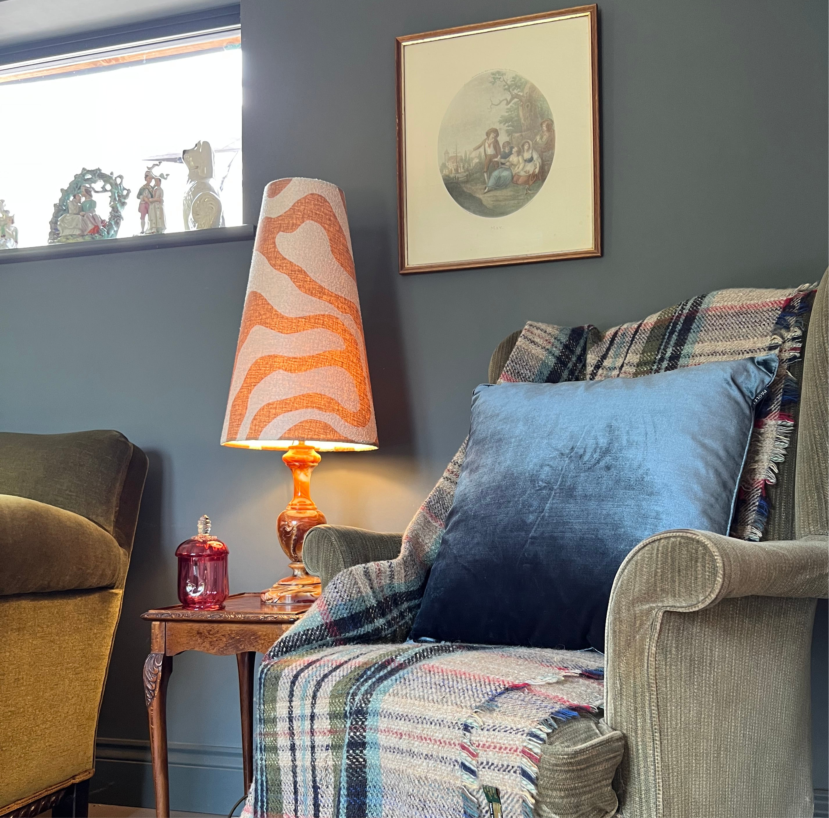 A warm-toned table lamp with an extra tall sandstone wiggle cone lampshade in wavy orange and cream patterns