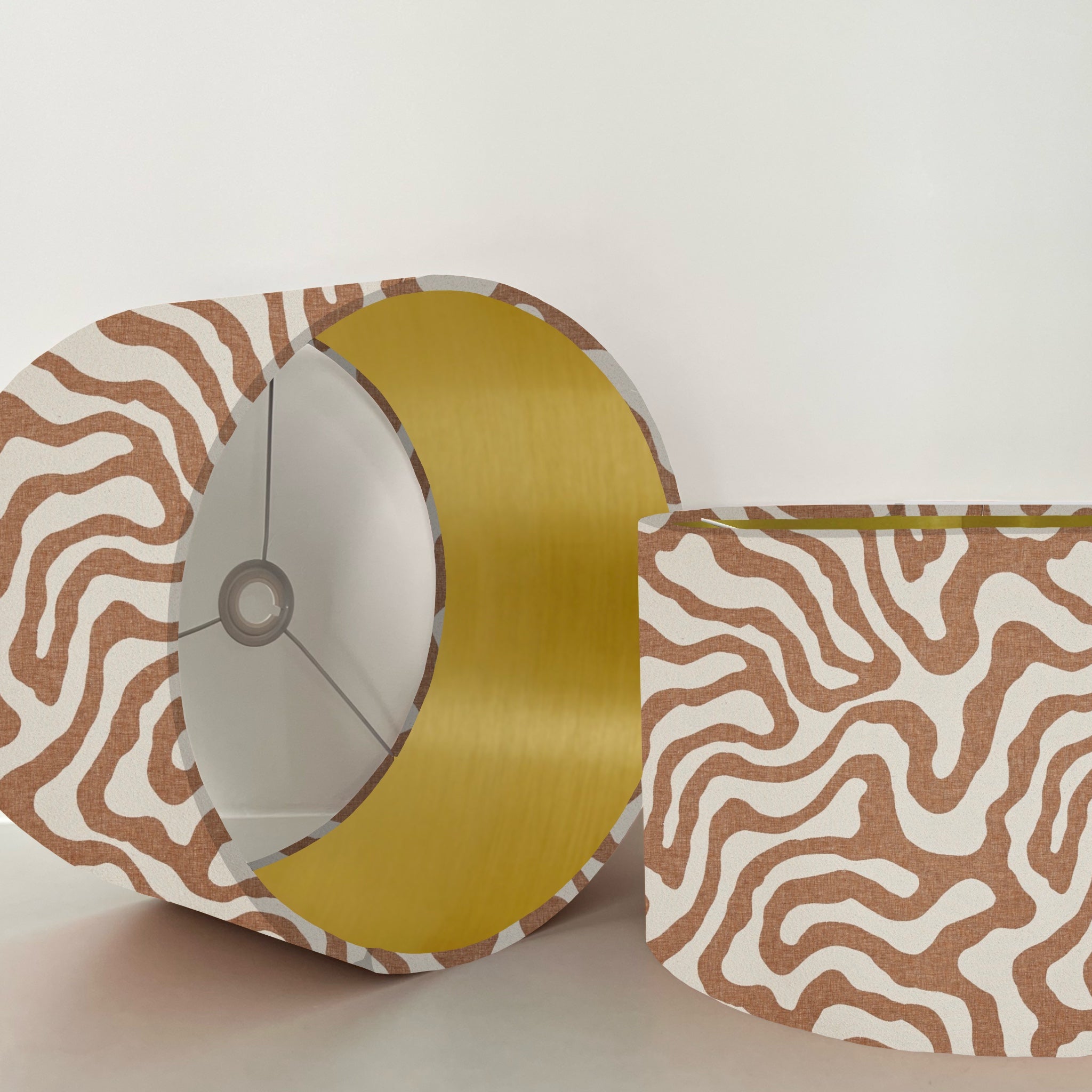 A sandstone wiggle drum lampshade with bold brown and white waves and a metallic brushed gold interior lining