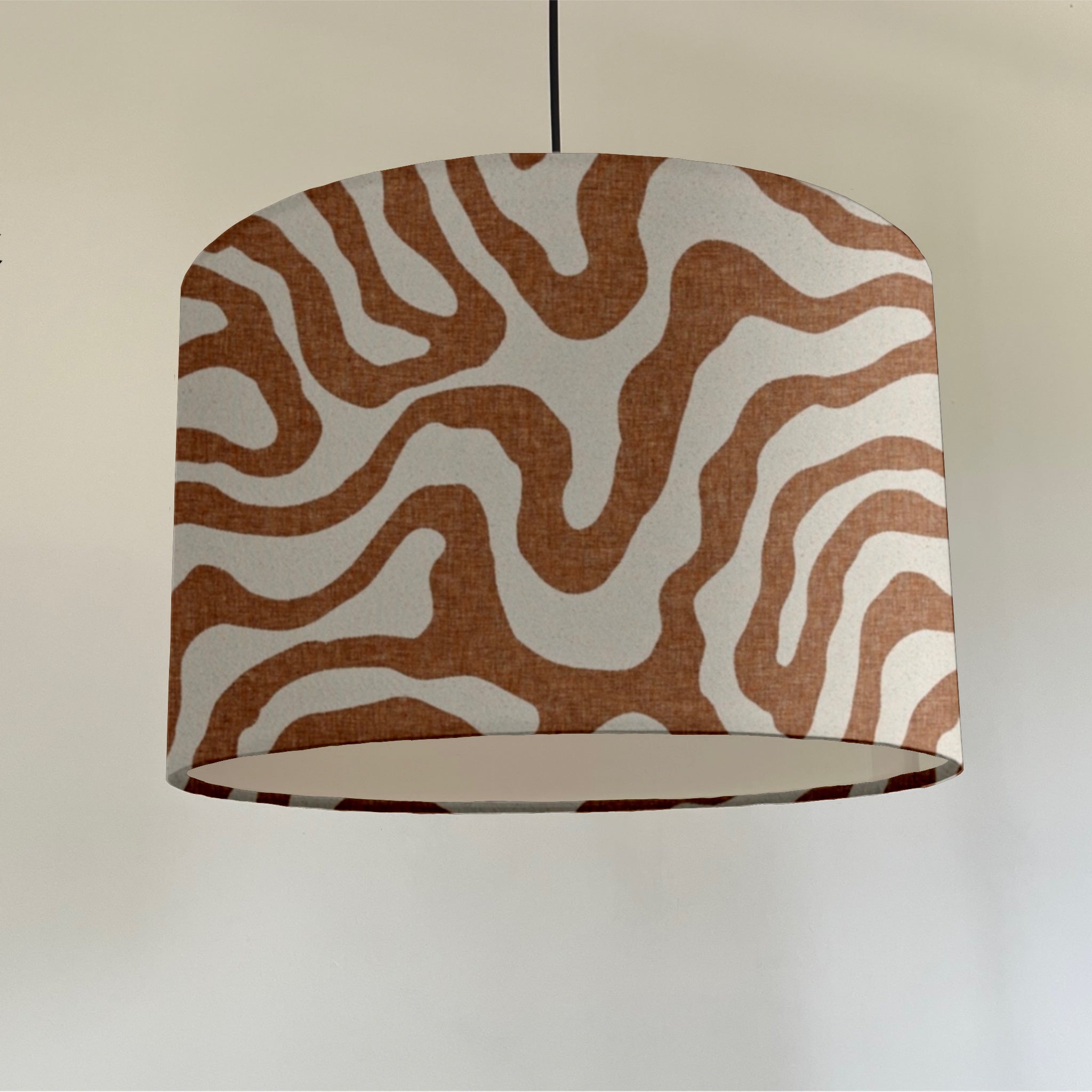 A cylindrical sandstone wiggle ceiling shade with bold wavy brown and white fabric and white lining fitting sits 3-4cm